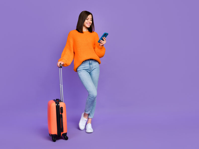 Image of a person with a small wheeled suitcase looking at thier smartphone