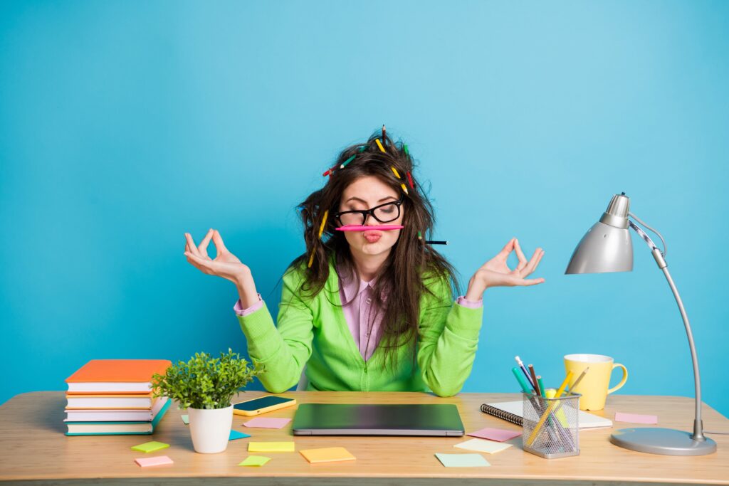 Picture of a woman sat at a desk meditating with a pen balnaced on their lip